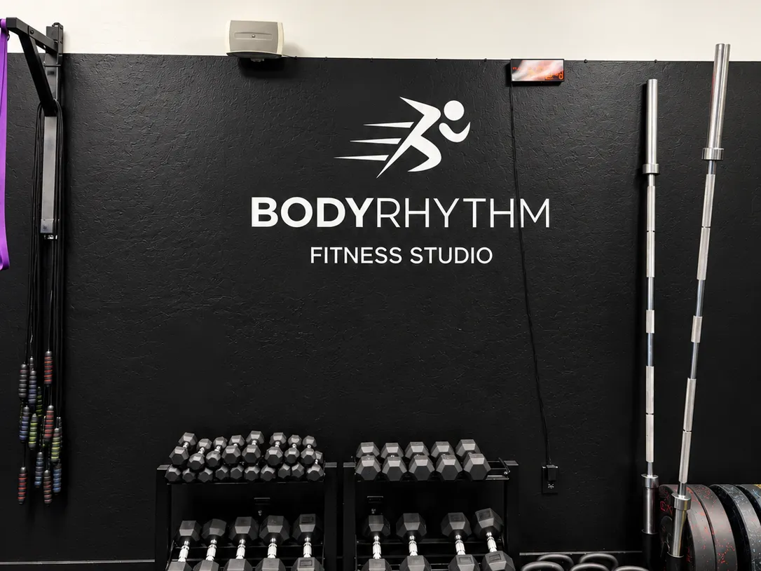 BodyRhythm logo wall with dumbbells and barbells